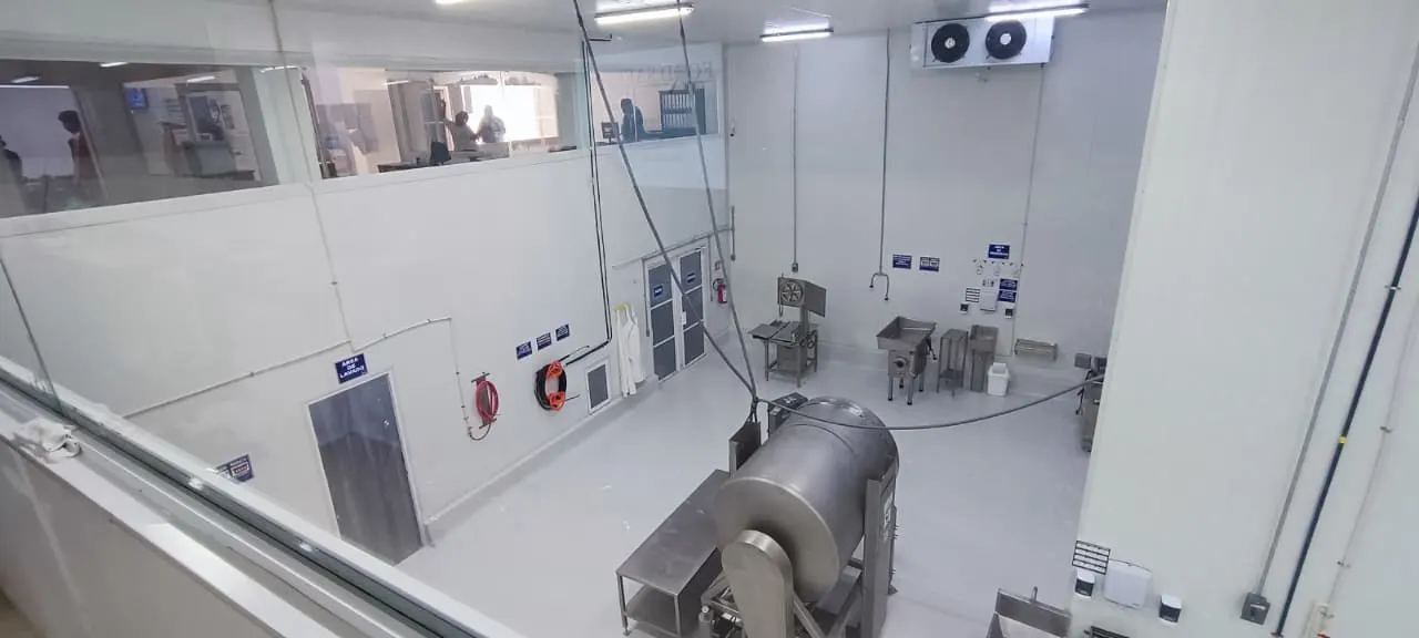 Línea de proceso con evaporador de refrigeración, molino de carne y acceso a cámara fría.